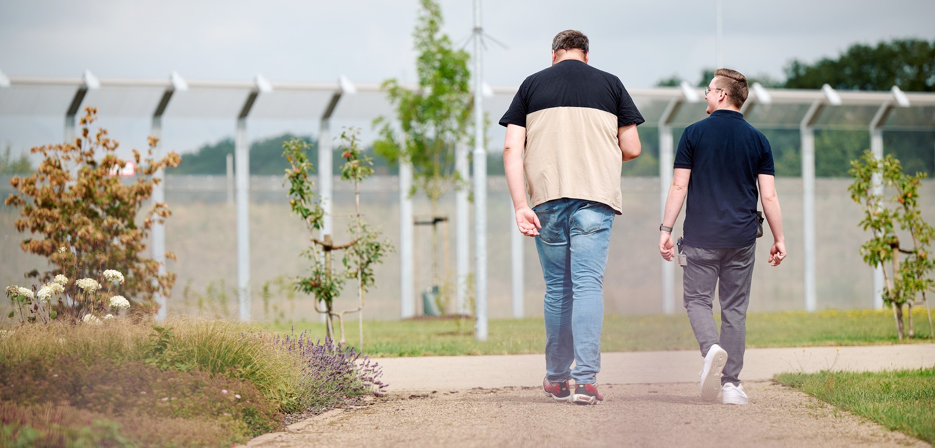 Zwei Männer gehen vor einem Hochsicherheitszaun spazieren
